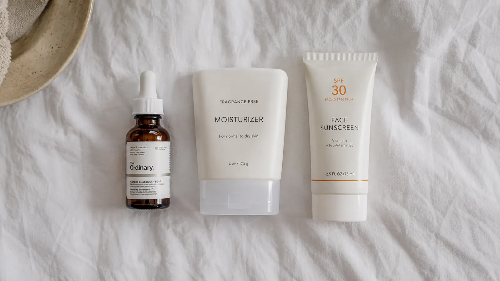 Flatlay of The Ordinary Niacinamide bottle alongside a moisturizer and SPF on a white linen surface